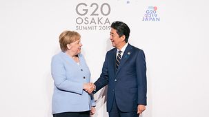 Bundeskanzlerin Angela Merkel wird beim G20-Treffen in Osaka von Japans Ministerpräsident Shinzo Abe begrüßt.