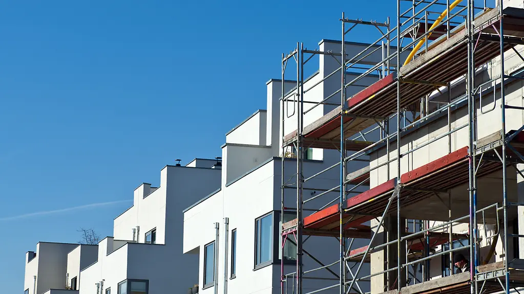 Ein eingerüsteter Neubau steht neben bereits fertig gestellten Häusern im Baugebiet.