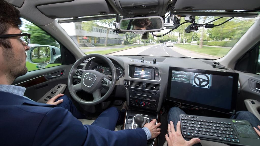 Ein Mann sitzt auf dem Fahrersitz und hält die Hände auf dem Schoß. Sein Beifahrer hat einen Laptop vor sich.