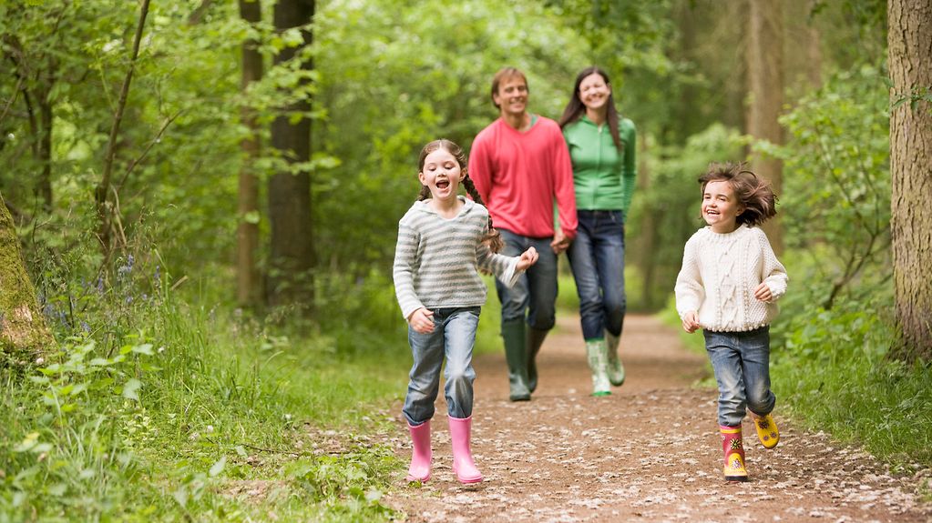 Eltern mit zwei Kindern gehen im Wald spazieren.