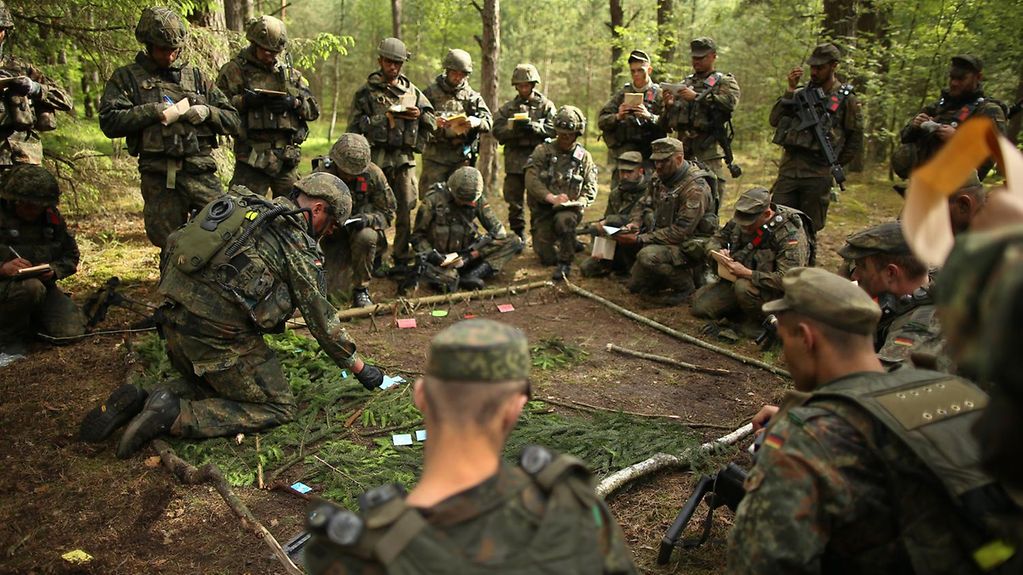 Soldaten in Tarnkleidung besprechen auf einer Waldlichtung die Lage. 