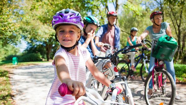 Familie mit Fahrrädern unterwegs in einem Park und alle tragen einen Fahrradhelm.