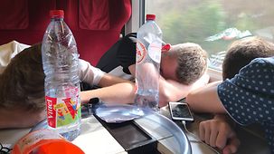 Drei junge Männer im Sitzen schlafend in einem Zugabteil