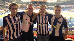 Vier junge Männer posieren in T-Shirts von Hertha BSC in einem Stadion