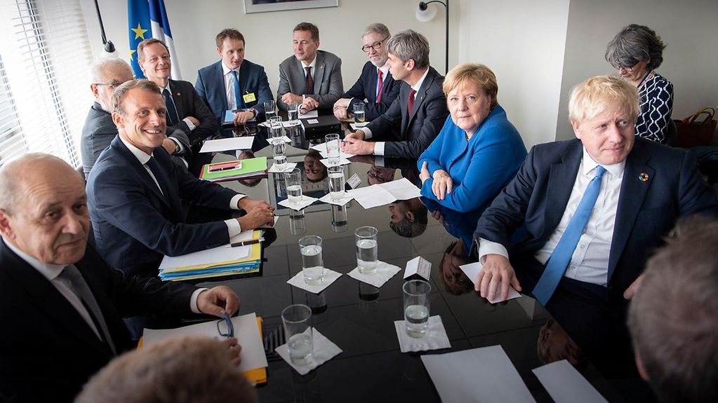 Kanzlerin Merkel sitzt mit Frankreichs Präsident Macron und dem britischen Premier Johnson an einem Besprechungstisch