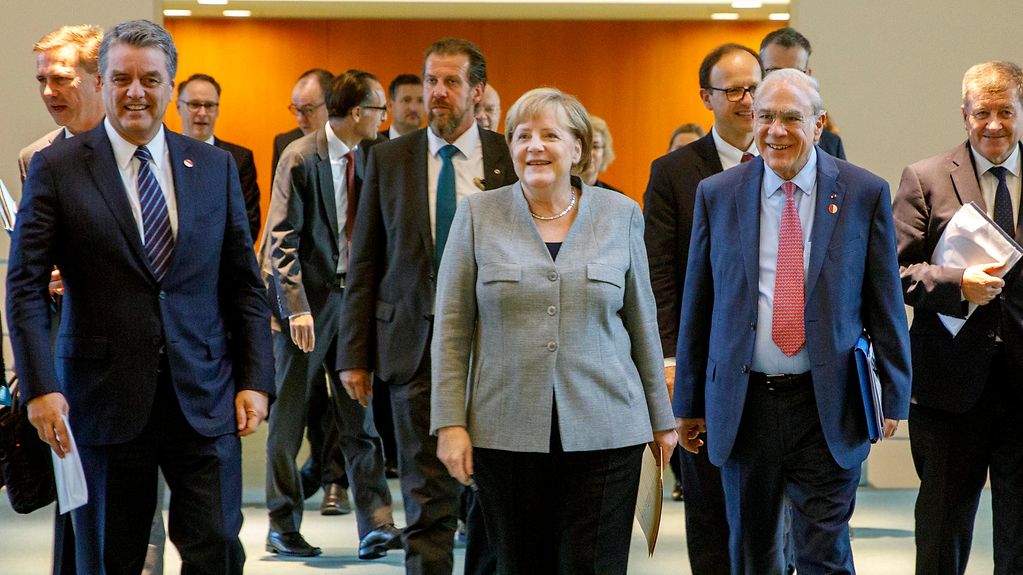 Bundeskanzlerin Angela Merkel geht zwischen Roberto Azevedo, Generalsekretär der WTO, und Jose Angel Gurria, Generalsekretär der OECD, zu einer gemeinsamen Pressekonferenz.