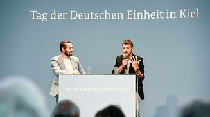 Christian Prokop und Moderator Sven Voss auf der Bühne der Bundesregierung beim Tag der Deutschen Einheit in Kiel.