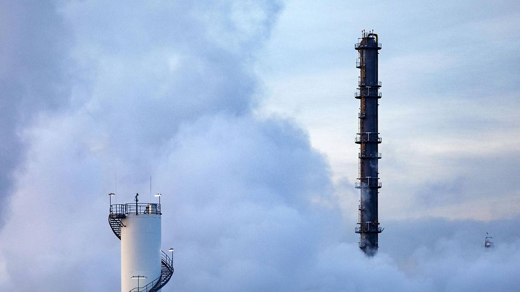Zwei Schornsteine von Industrieanlagen brechen durch eine Wolken-Rauch-Decke.