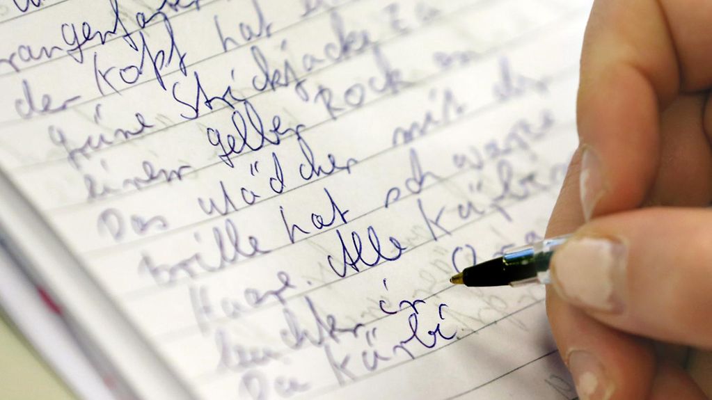Eine Frauenhand schreibt mit Kugelschreiber einen Text auf ein liniertes Blatt Papier.