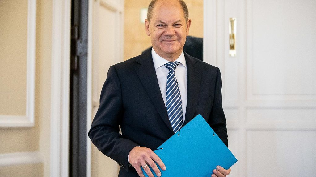 Bundesfinanzminister Scholz betritt den Presseraum des Bundesfinanzministeriums und hält dabei eine blaue Mappe in der Hand.