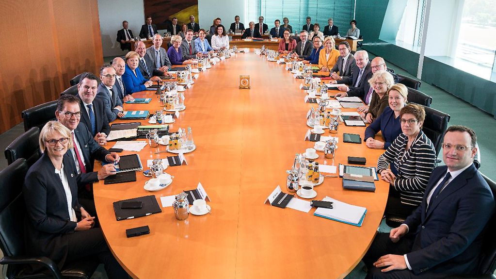 Am Kabinettstisch sitzen sämtliche Bundesministerinnen und Bundesminister des Kabinetts. Im Hintergrund sind Vertreter der Presse zu sehen.