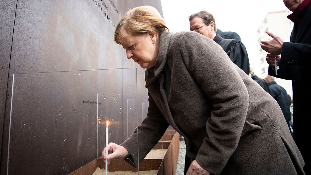 The photo shows the Chancellor lighting a candle in memory of the victims.
