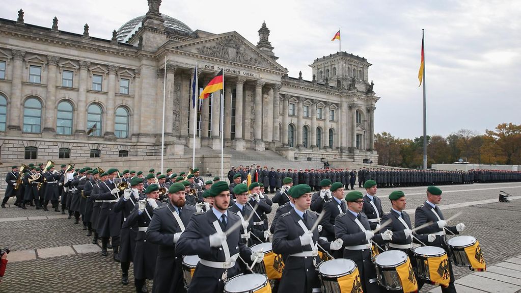 Ein Musikkorps der Bundeswehr marschiert vor dem Bundestag ein, vorneweg gehen Soldaten mit gelben Trommeln.