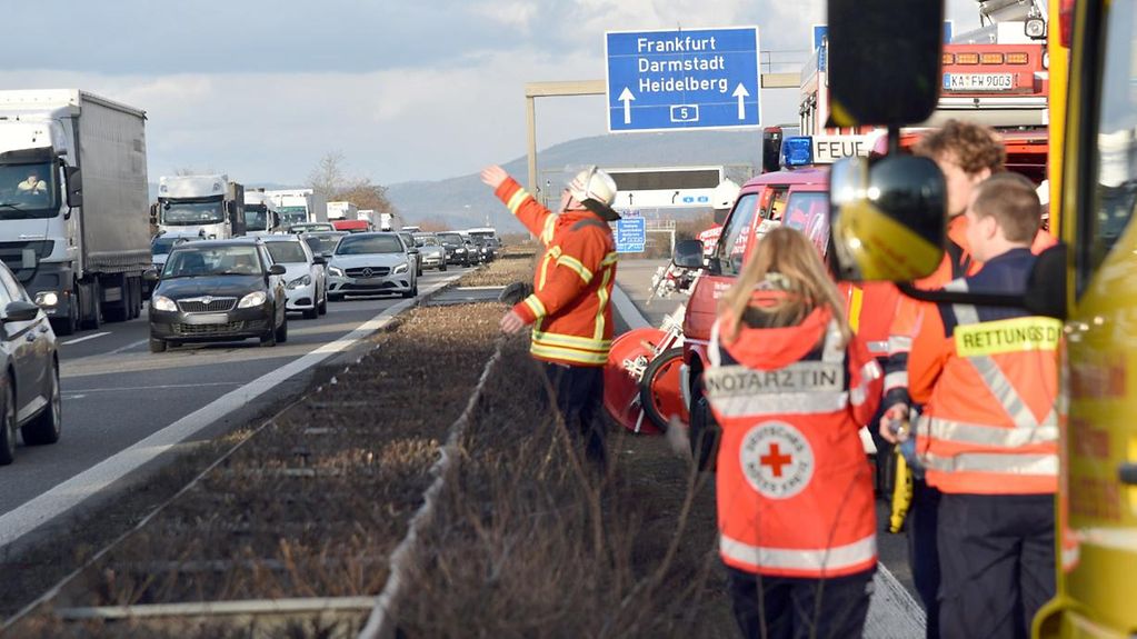 Rettungskräfte sichern eine Unfallstelle auf einer Autobahn, ein Feuerwehrmann winkt in Richtung Gegenfahrbahn.