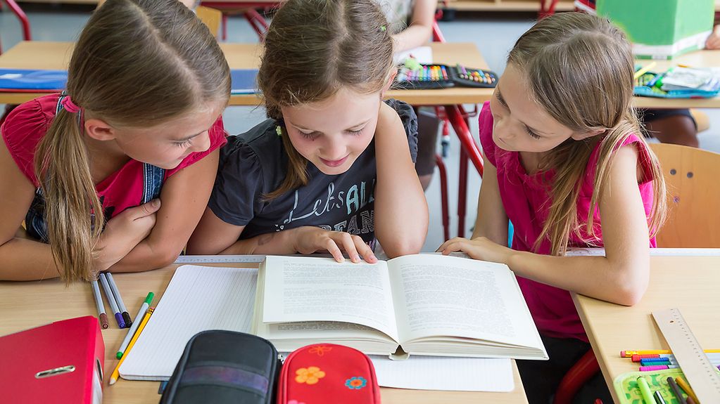 Drei Grundschülerinnen lesen in einem Schulbuch.