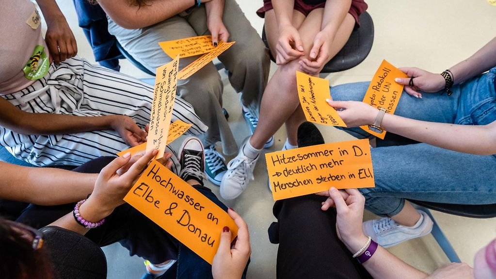 Teilnehmer des Klimaworkshops sitzen im Kreis und halten orangene Karteikarten mit Stichworten zum Klimawandel in ihren Händen.