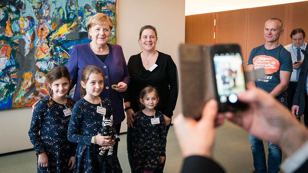 Bundeskanzlerin Angela Merkel macht mit einer Familie ein Erinnerungsfoto.