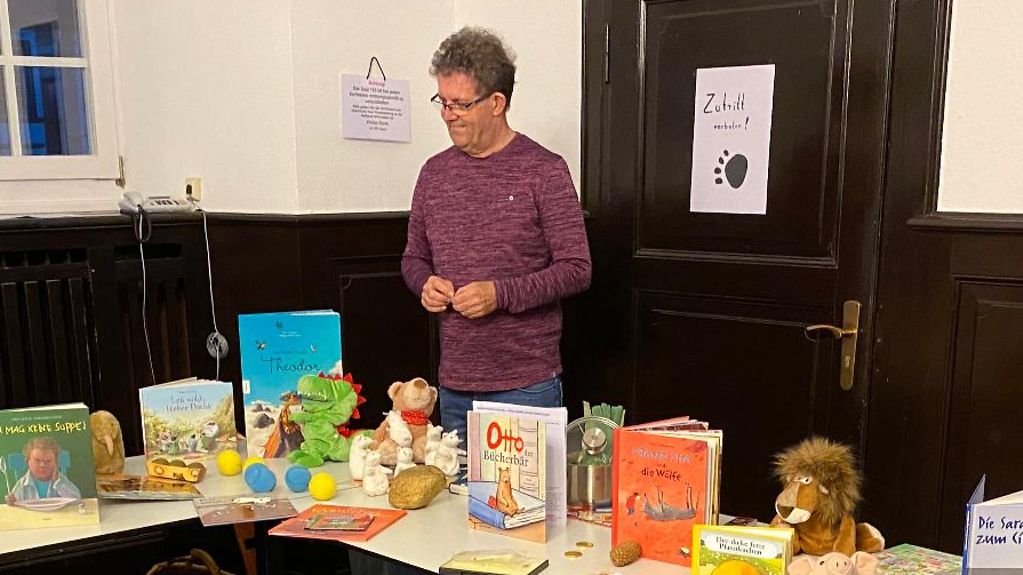 Der ehrenamtliche Vorlesepate Ulf Störmer steht in einem Klassenraum hinter einem Tisch mit Kinderbüchern.