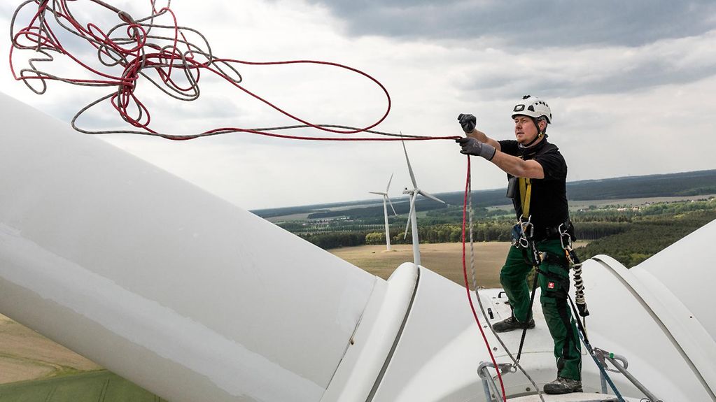 Industriekletterer prueft Rotorblatt von Windkraftanlage um Schaeden zu erkennen, oder vor Ort zu reparieren 