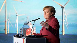 Chancellor Angela Merkel at the lectern, behind her an image of offshore wind turbines and a ship