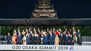Family photo with all participants of the summit. In the background stands an imposing pagoda. At the bottom stands "G20 Osaka Summit 2019" with the summit logo.