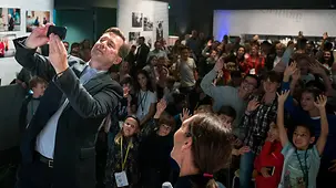 Federal government spokesperson Steffen Seibert takes a selfie with children, who are happily waving their arms in the air.