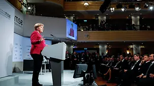 Chancellor Angela Merkel at a lectern on stage in the Hotel Bayerischer Hof during the Munich Security Conference. In the background we see the conference logo.