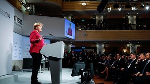 Chancellor Angela Merkel at a lectern on stage in the Hotel Bayerischer Hof during the Munich Security Conference. In the background we see the conference logo.