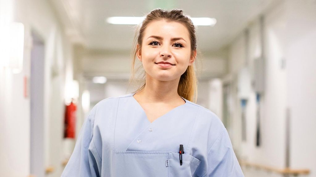 Auszubildende Michelle Gagala steht im hellblauen Kittel in einem Krankenhausflur.