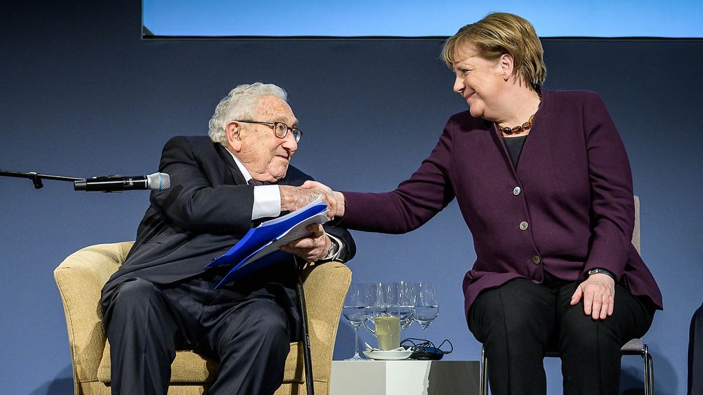 Henry Kissinger, former US Secretary of State, congratulates Chancellor Angela Merkel on the stage.
