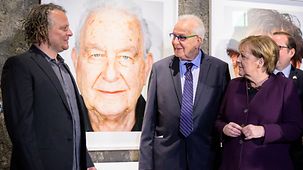 La chancelière fédérale Angela Merkel aux côtés de Naftali Fürst et de l’artiste Martin Schoeller lors de l’inauguration de l’exposition « Survivors »