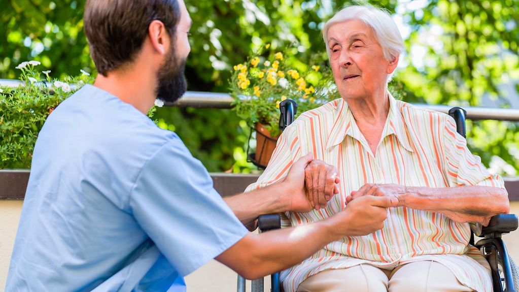 Ein Pfleger hält die Hände einer Seniorin im Altersheim.