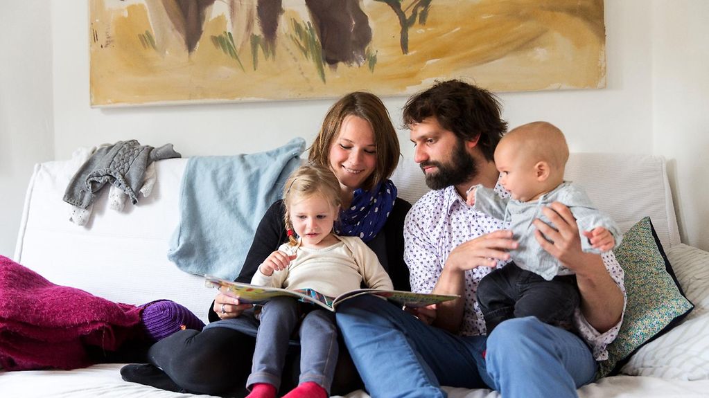 A young family reads a storybook together on the sofa.