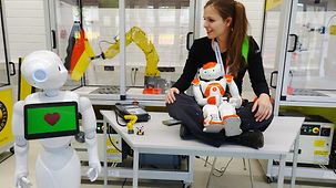 Die Mechatronikstudentin sitzt auf einem Tisch und ihrem Schoß liegt ein Roboter.