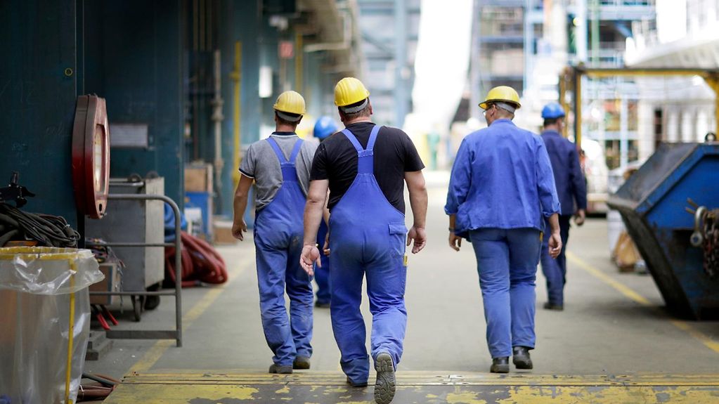Industrial workers walk through a production hall.
