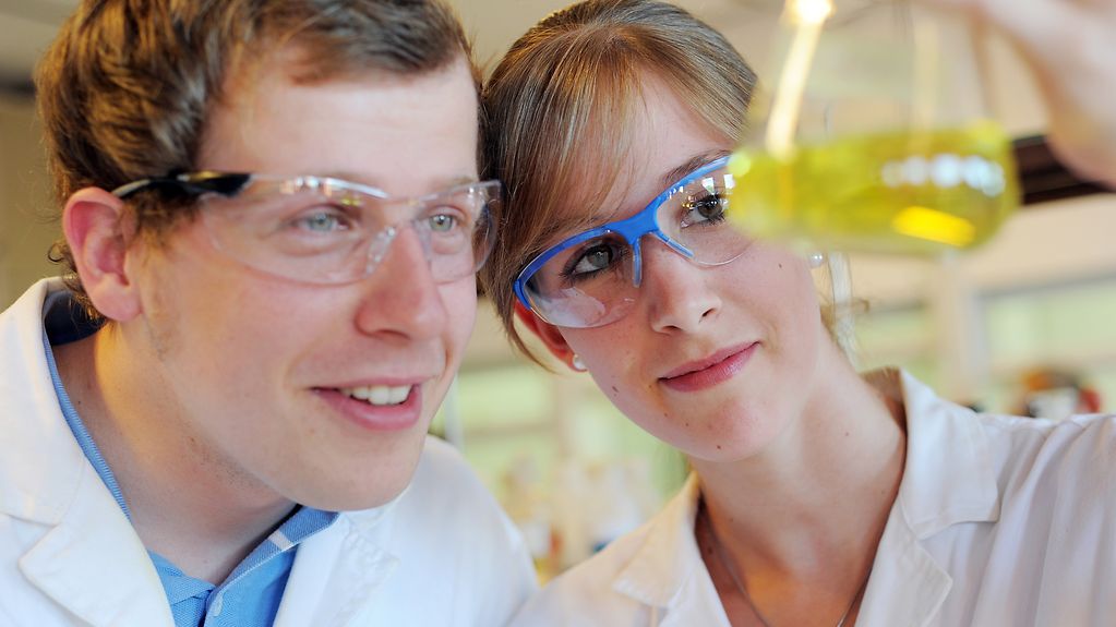 Wissenschaftliche Mitarbeiter schauen sich eine chemische Flüssigkeit durch Schutzbrillen an.