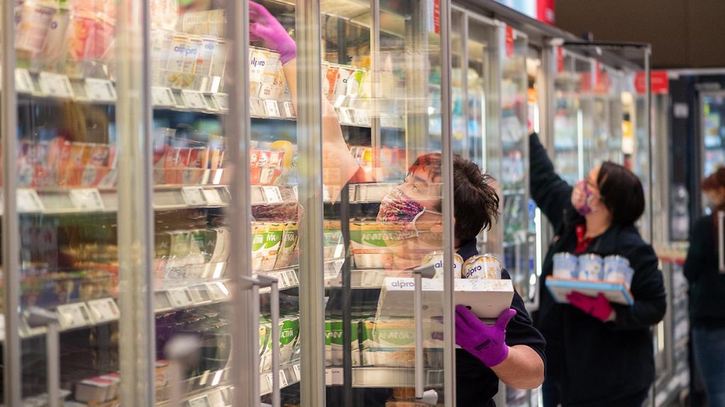 Mitarbeiterinnen in einem Supermarkt tragen Schutzmasken, während sie Regale auffüllen.