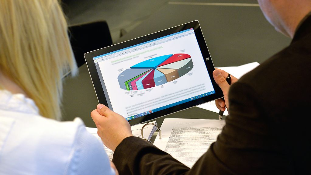 Hands holding a tablet PC on which a pie chart can be seen.