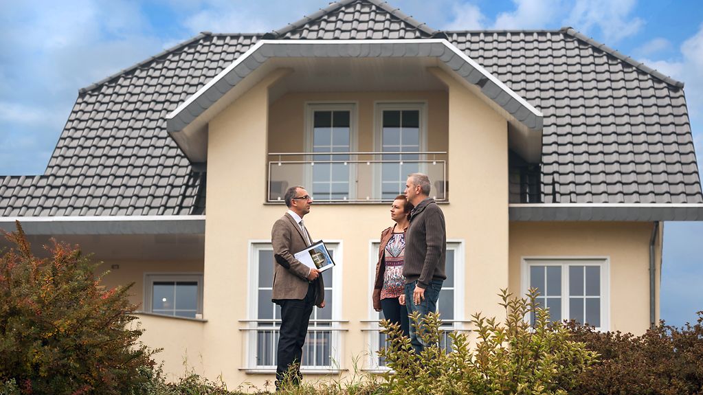 Immobilienmakler kommuniziert mit potentiellen Käufern vor Wohnhaus.