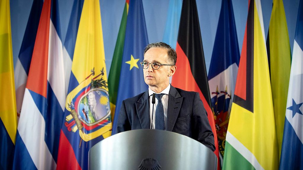 Außenminister Heiko Maas steht vor einer Wand aus Flaggen an einem Pressepult.