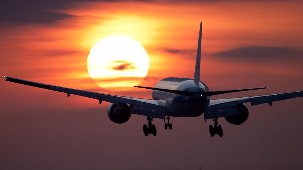 Das Bild zeigt ein fliegendes Flugzeug vor dem Sonnenuntergang.