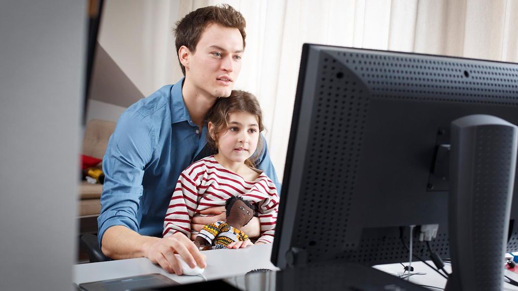  Ein junger Mann sitzt mit einem jungen Mädchen an einem Schreibtisch und schaut auf einen Computer. 