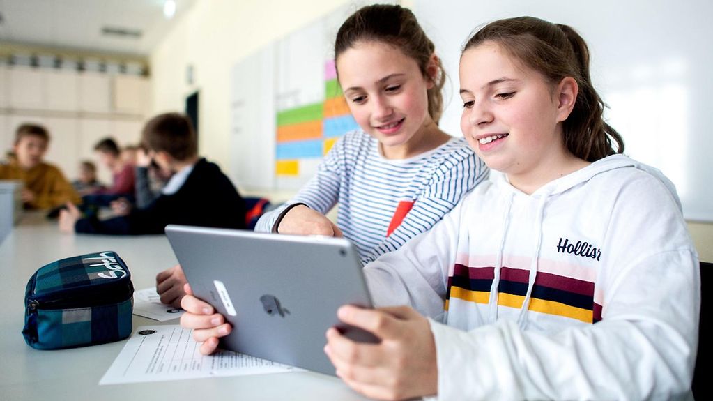 Zwei Schülerinnen benutzen in der Schule gemeinsam ein Tablet.
