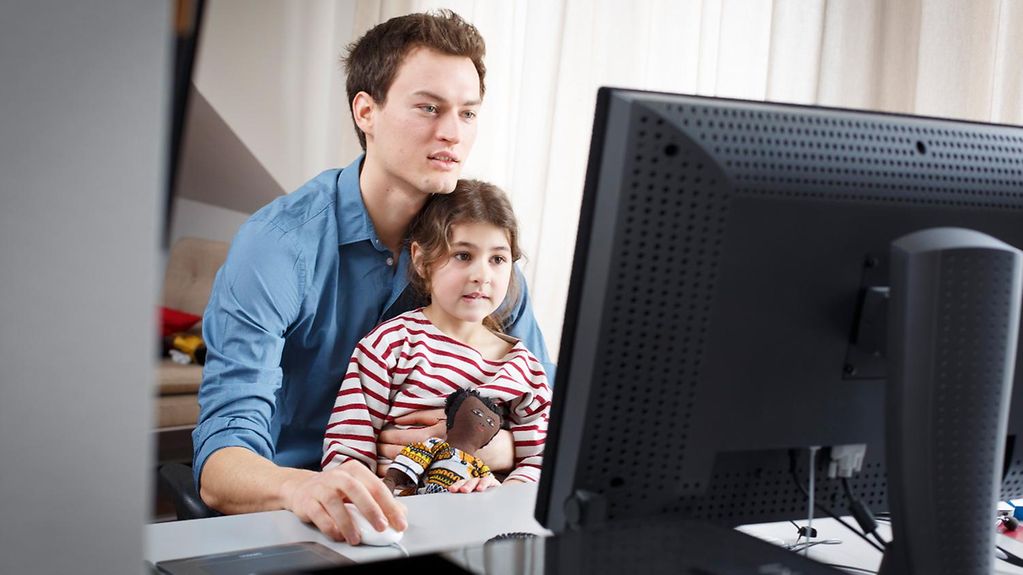 Un jeune homme assis devant un ordinateur avec une petite fille