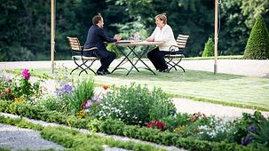 Chancellor Angela Merkel and French President Emmanuel Macron sit at a table in the grounds of Schloss Meseberg.