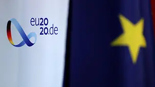 Logo der deutschen EU-Ratspräsidentschaft und Europa-Fahne im Vordergrund.