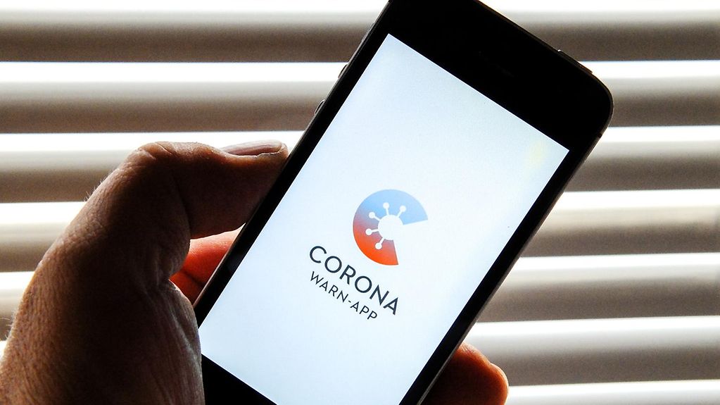 Ein Mensch hält sein Smartphone, auf dem die Corona-Warn-App geöffnet ist.