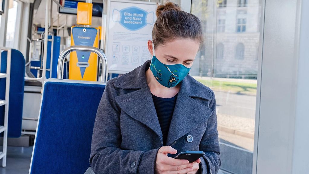 Eine Frau mit Mund-Nasen-Bedeckung sitzt in einer Straßenbahn.