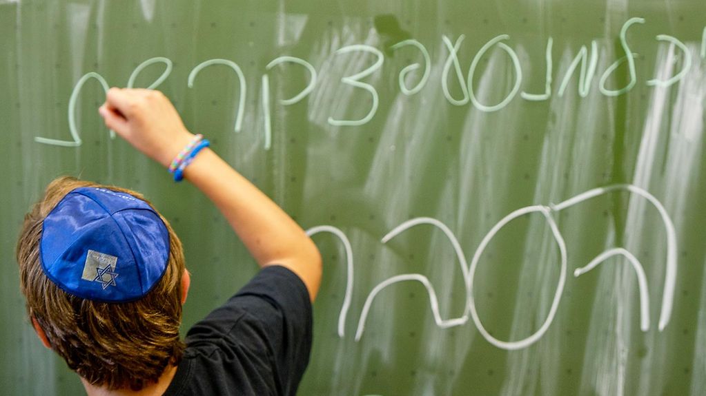 Ein Schüler schreibt das Alphabet auf Hebräisch an eine Tafel. 