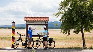 Paar mit Fahrrädern, neben Grenzstein